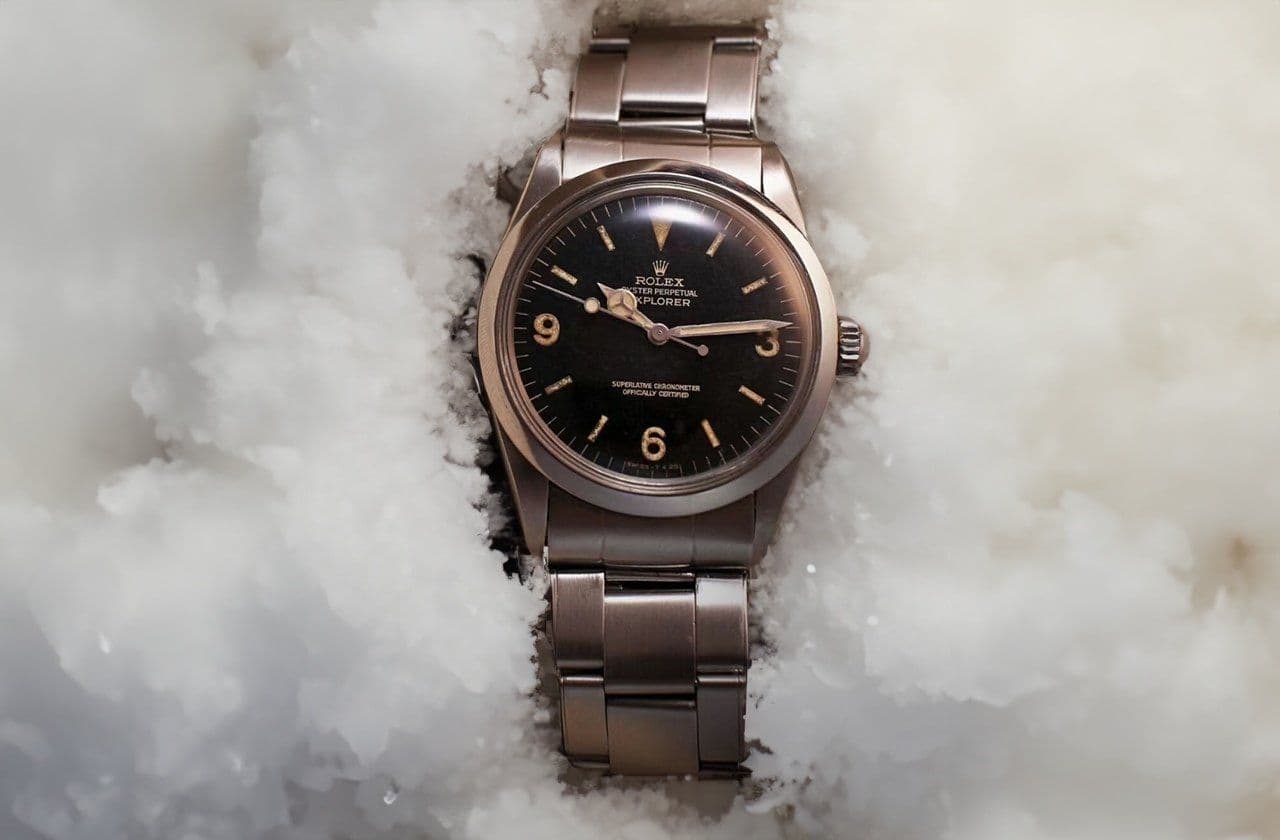 A Rolex Explorer watch with a black dial and stainless steel bracelet resting in snow, symbolizing its durability for extreme adventures like Mount Everest climbs.